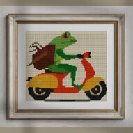 frog-on-scooter alternative framed cross stitch mockup, realistic finished embroidery presentation